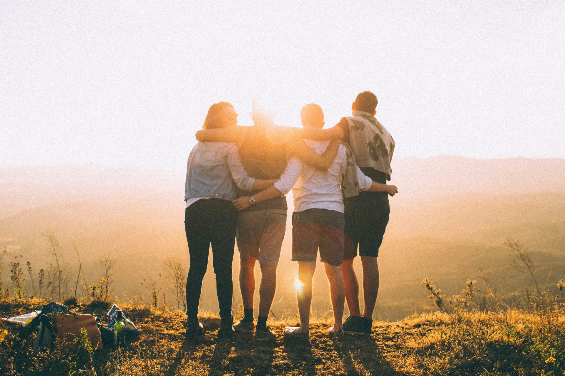 Vier Personen legen die Hände um die Schultern und betrachten den Sonnenuntergang.